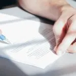 Dłonie podpisujące umowę długopisem na biurku.
